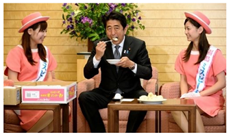 Japanese Prime Minister Shinzo Abe eating a peach grown in Fukushima, assisted by two Fukushima residents